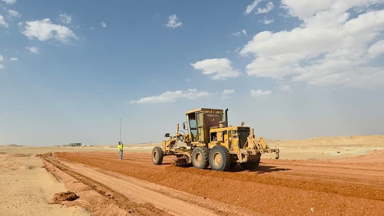 جريدر يسوّي ممر الطريق ومساح يقف على جانبه