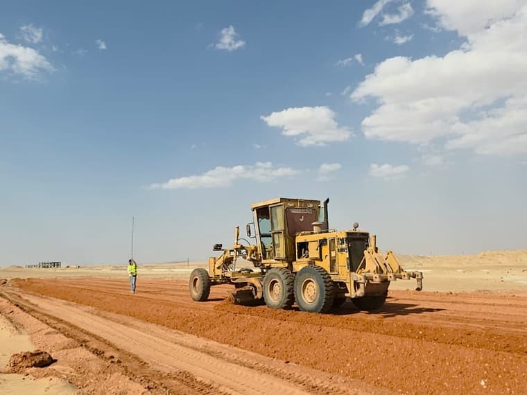 جريدر يسوّي ممر الطريق ومساح يقف على جانبه